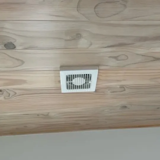 A small white ceiling vent fan set into a timber ceiling.